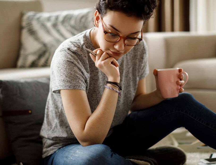 a woman with a writing pen in her hand looking at her laptop while drinking coffee
