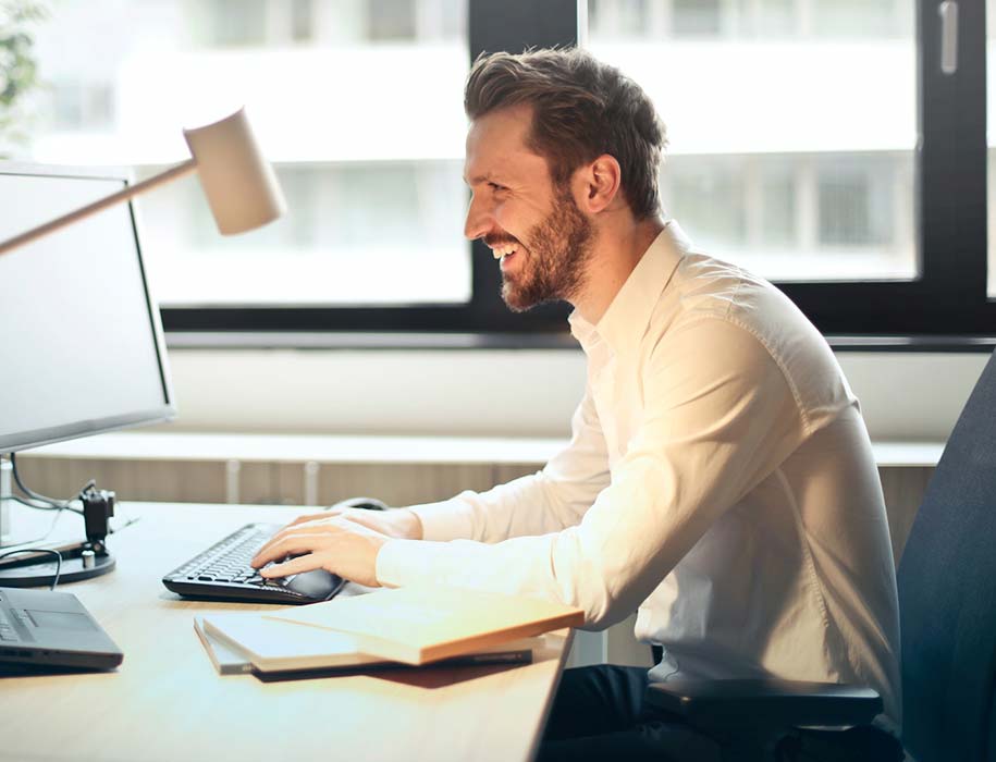 Man sitting at desk in office typing at computer.