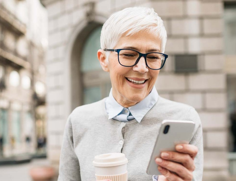 a mature woman wearing glasses and holding her mobile phone with her cup of coffee