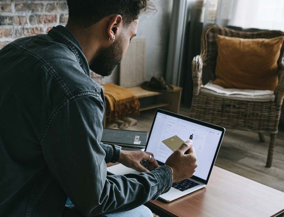 Man at home holding credit card and using laptop.
