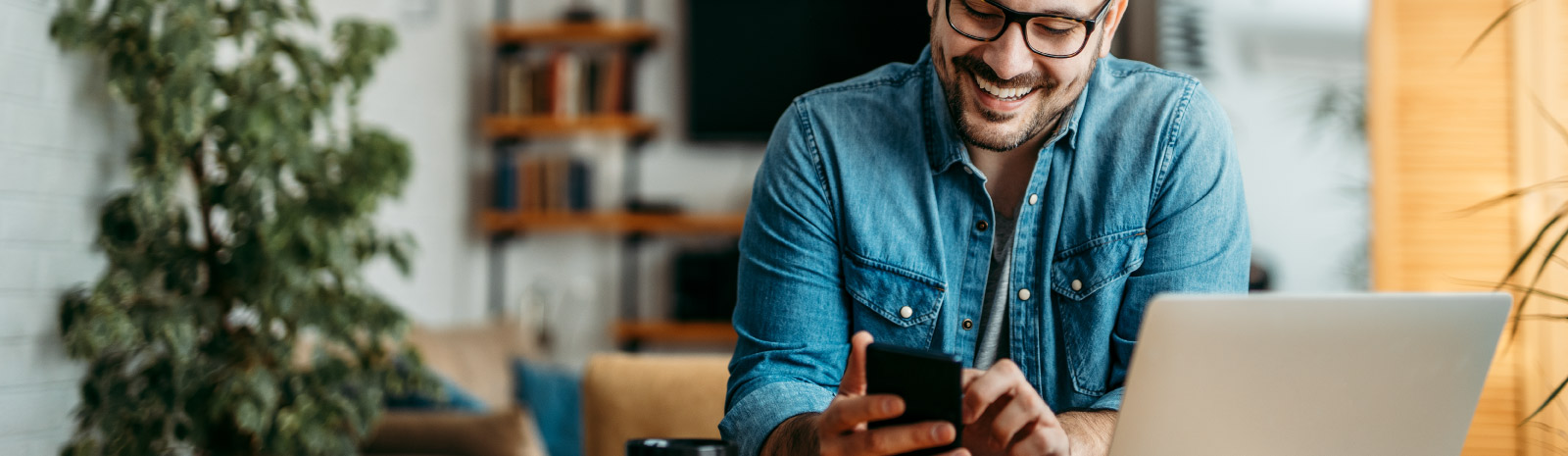 Man at home using phone in front of laptop.